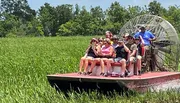 A group of people are taking a ride through a grassy wetland on an airboat.