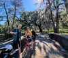 Two people are riding bicycles through a scenic park with large trees draped in Spanish moss