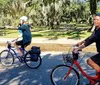 Two people are riding bicycles through a scenic park with large trees draped in Spanish moss