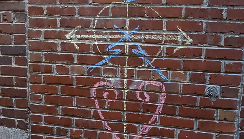 The image shows a brick wall with simple drawings in chalk including a pink ice cream cone blue lines and other abstract shapes