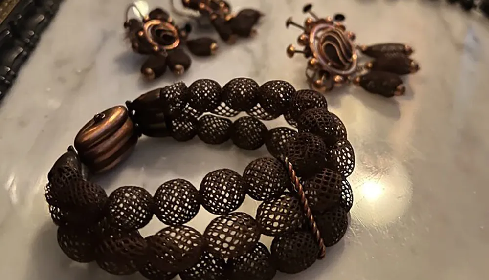 The image features a close-up view of a dark textured bracelet paired with matching earrings on a reflective surface