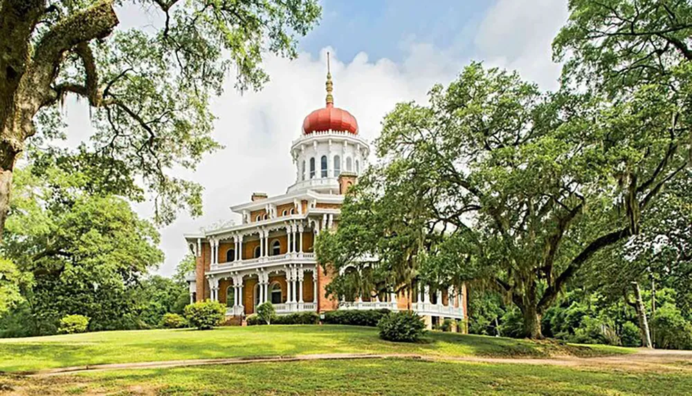 The image shows a grand historic mansion with a distinctive red-domed cupola surrounded by lush greenery and aged trees draped with Spanish moss