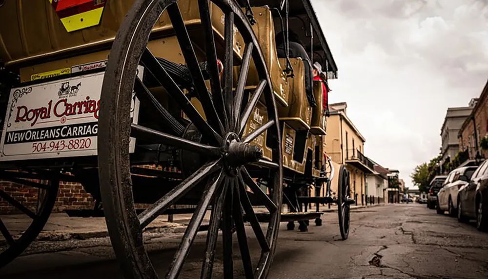 A horse-drawn carriage with prominent wheels is parked on a street lined with cars and historic buildings conveying a mix of old charm and modern life