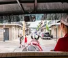 A carriage driver in a red shirt and white cap looks ahead as the horse pulls the carriage along a street lined with buildings and vehicles