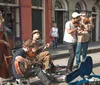 A group of musicians is performing live on a city street with instruments like a double bass guitar violin and clarinet as bystanders watch and a guitar case lies open to collect tips