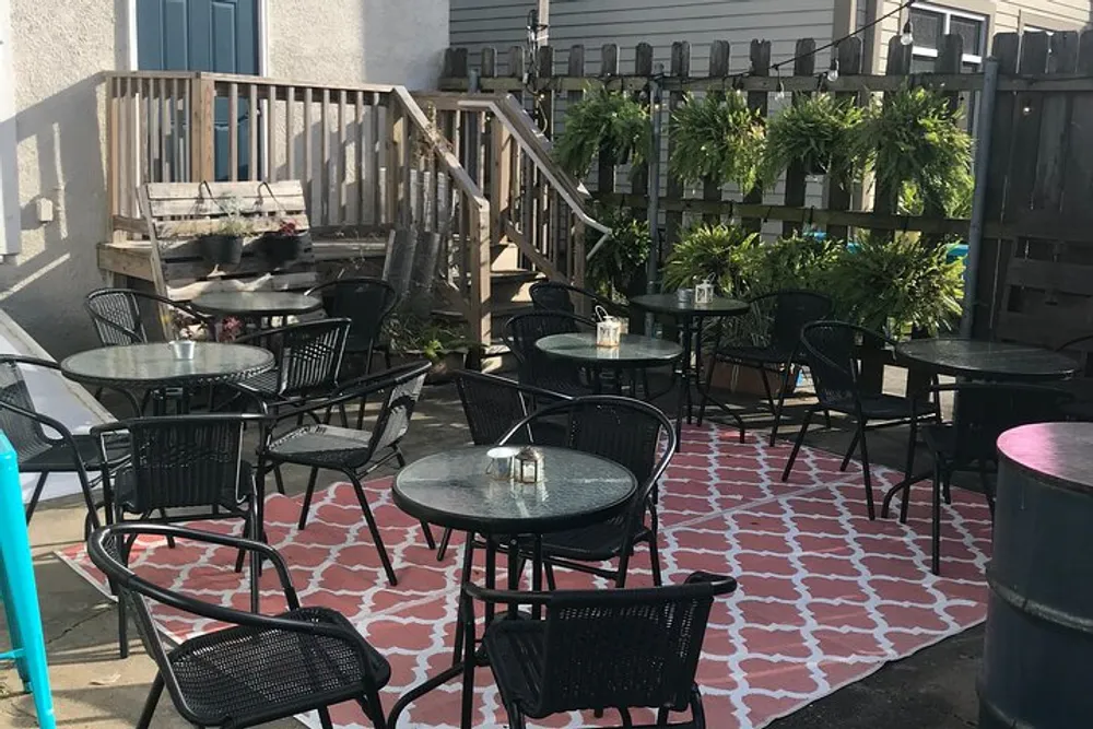 The image shows an outdoor patio area with multiple tables and chairs patterned flooring potted plants along a fence and a staircase leading to a building