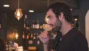 A man is sipping a cocktail in a dimly lit bar.