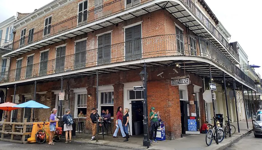 This image shows people casually enjoying their day outside a brick building with balconies, characteristic of the historic architecture one might find in the French Quarter of New Orleans.