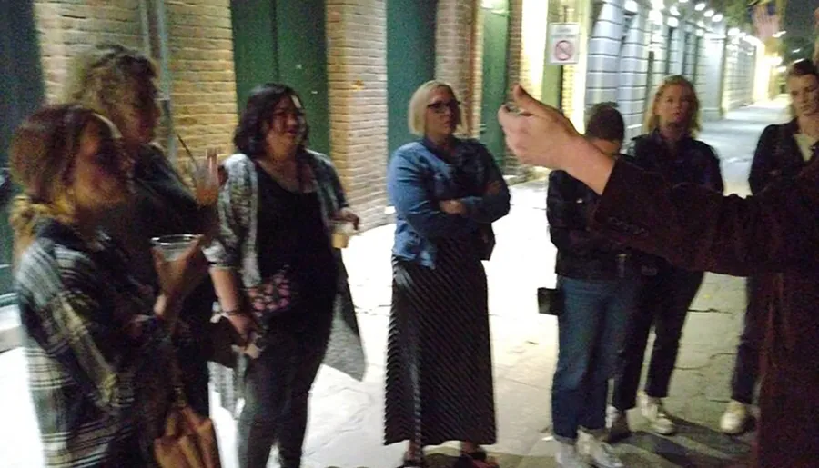 A group of people is engaged in an animated conversation on a street at night, with one person gesturing while speaking.