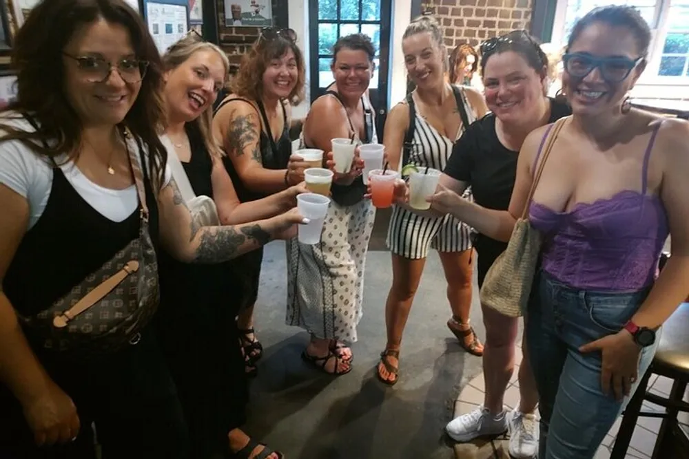 A group of smiling women are toasting with drinks inside a casual venue