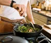 A person is chopping herbs on a wooden cutting board in a well-equipped kitchen