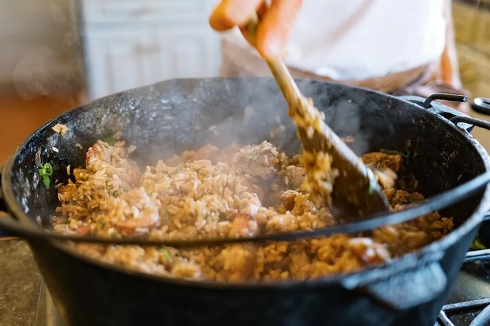 A person is stirring a large pot of steaming food likely some type of rice dish on a stove