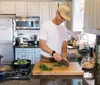 A person is chopping herbs on a wooden cutting board in a well-equipped kitchen