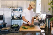 A person is chopping herbs on a wooden cutting board in a well-equipped kitchen.