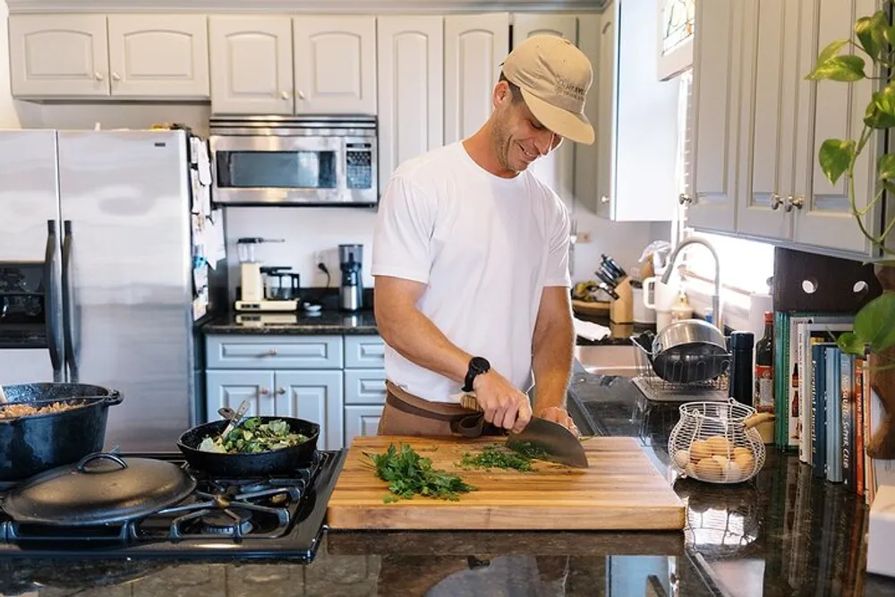 A person is chopping herbs on a wooden cutting board in a well-equipped kitchen