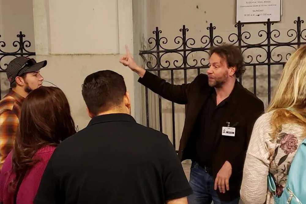 A group of people is attentively listening to a man who is pointing upwards likely giving a tour or explanation about the place they are visiting