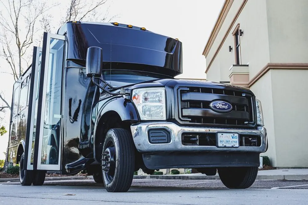 A black Ford truck with an unconventional vertical lift door is parked near a building