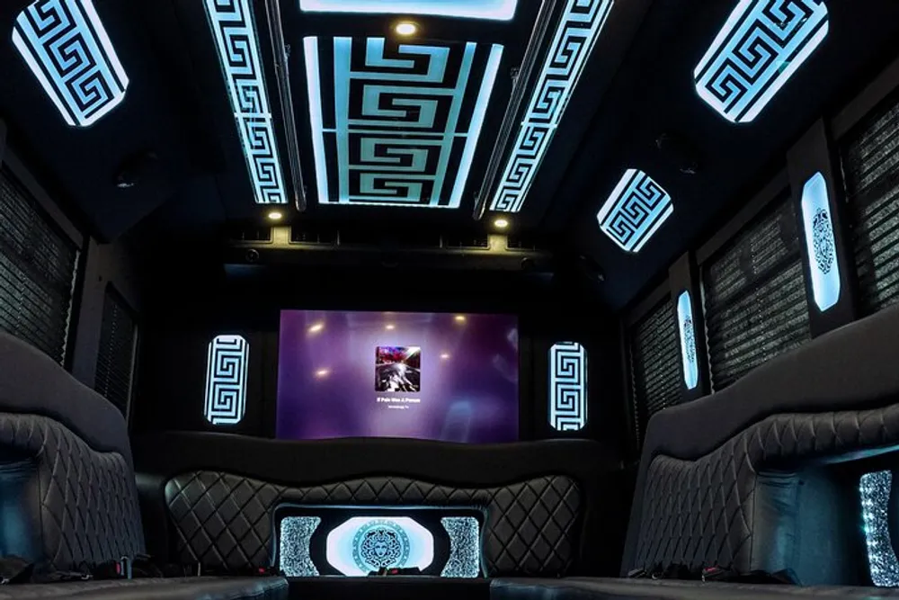 The image shows a luxurious and modern interior of a vehicle possibly a limousine with a Greek key design motif illuminated along the walls and ceiling comfortable seating and a large screen on the front wall