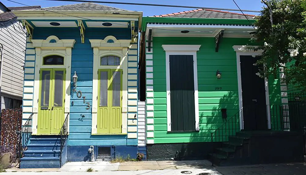 The image shows two colorful adjacent shotgun houses with distinctive blue and green exteriors and decorative trim in a style characteristic of New Orleans architecture