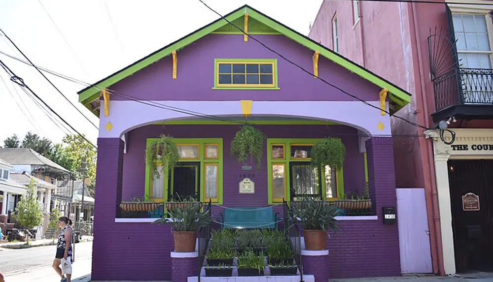 The image shows a vibrant purple house with green highlights and a person walking by on a sunny day