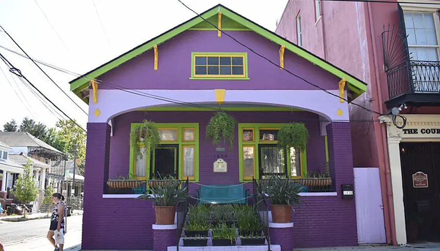 The image shows a vibrant purple house with green highlights and a person walking by on a sunny day.