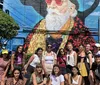 A group of people is posing for a photo in front of a colorful mural featuring a large depiction of an elderly man with a beard and sunglasses