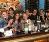 A group of people is posing with smiles behind a bar counter cluttered with cocktail-making equipment and glasses