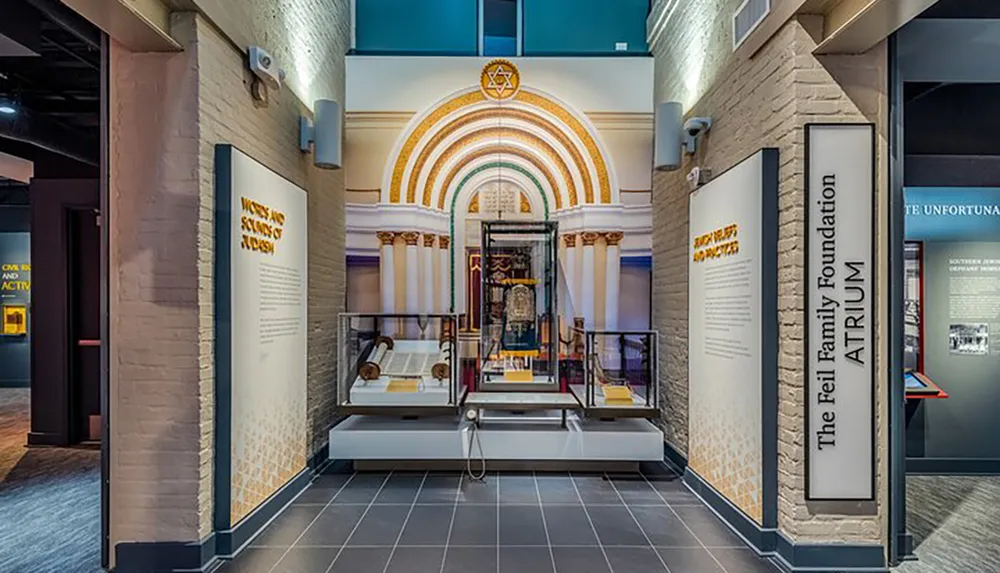 The image showcases an exhibit hall within a museum featuring an arched display with a decorative mosaic and historical artifacts presented in glass cases designed to impart educational content to visitors