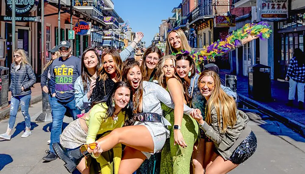 A group of cheerful people is posing for a photo on a lively street with one individual prominently displaying a bride-to-be sash