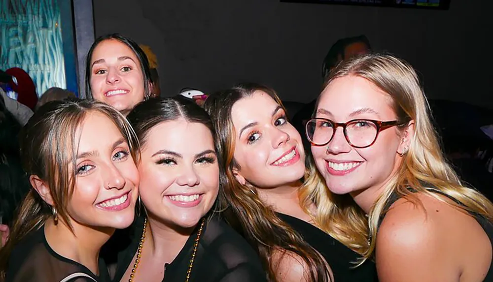 Five young women are posing closely together with smiles seemingly enjoying a social event