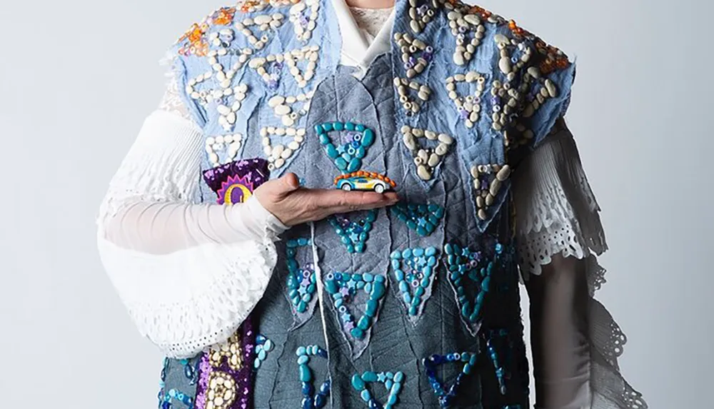 A person is wearing an ornate jeweled vest over a white blouse with ruffled sleeves striking a fashionable pose