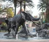 The image captures a dynamic fountain display featuring statues of elephants and lions surrounded by water jets set in a serene landscape with palm trees and a clear sky