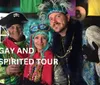 Three people are dressed in colorful and flamboyant costumes possibly for a festival or themed event with the words GAY AND SPIRITED TOUR overlaid on the image