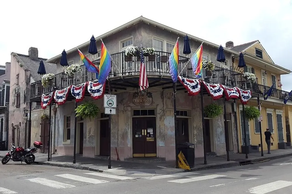 The image displays a weathered corner building adorned with both rainbow pride flags and American patriotic bunting suggesting a celebration of diversity and national pride