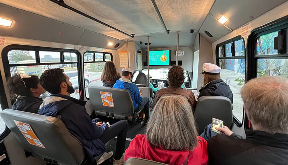 Passengers are seated inside a bus looking forward as they appear to be in transit or awaiting departure