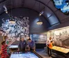 A group of people explore a museum exhibit featuring historical photographs and interactive displays in a dimly lit arched room