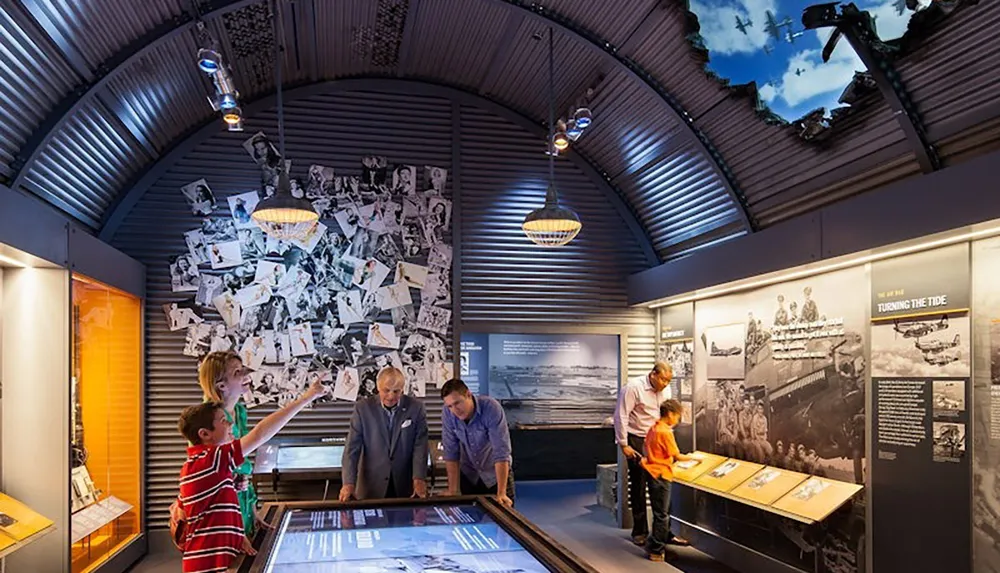 A group of people explore a museum exhibit featuring historical photographs and interactive displays in a dimly lit arched room