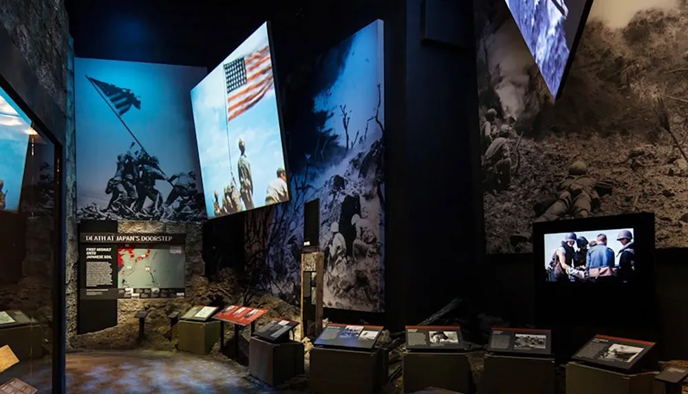 The image depicts a museum exhibit featuring large historical photographs and displays relating to the military including the iconic raising of the American flag