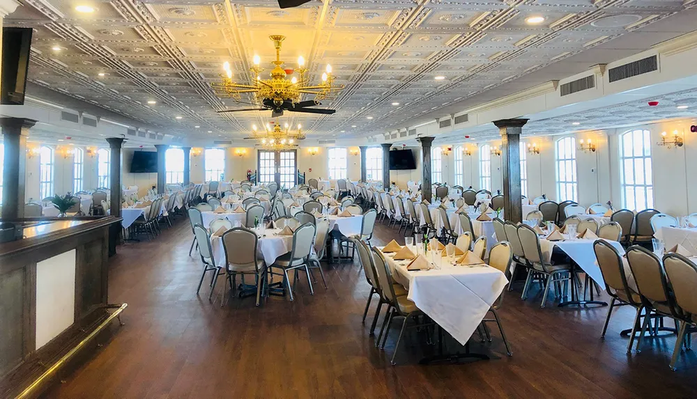 A spacious and elegantly decorated banquet hall is set with white tablecloths and neatly arranged chairs