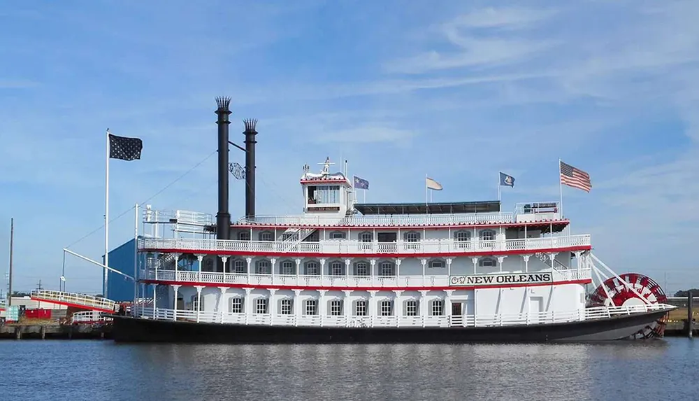 The image shows a white and red paddle steamboat named New Orleans with multiple flags docked on a body of water