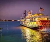 A brightly lit riverboat cruises along a calm river at dusk with an inset image showing people enjoying a lively band performance inside