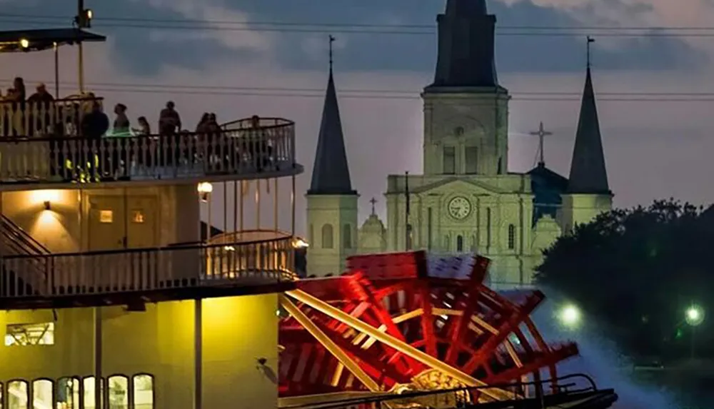 A paddle steamboat sails in front of a historic cathedral at dusk