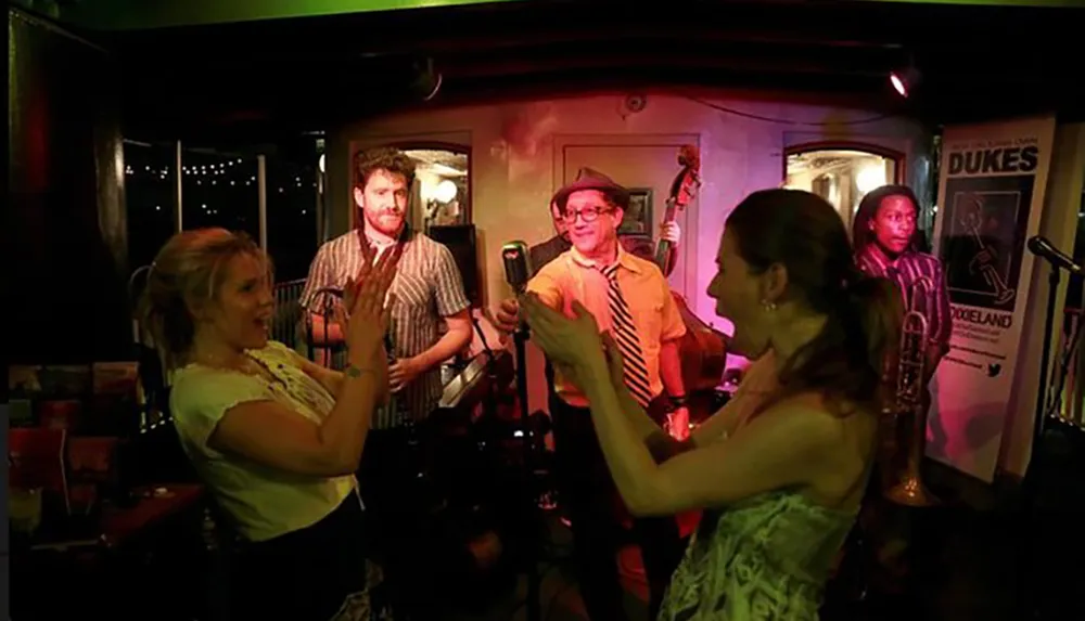 A group of people enjoy a lively performance at a dimly lit venue with musicians and audience members interacting cheerfully