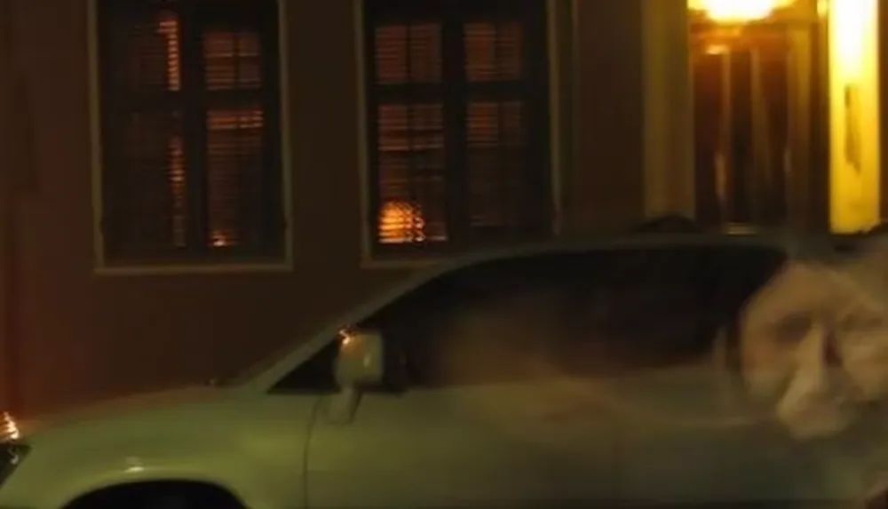 A car is parked in front of a building with illuminated windows at night