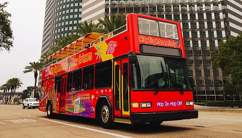 A brightly colored double-decker bus labeled CitySightseeing New Orleans is driving through a city street lined with palm trees