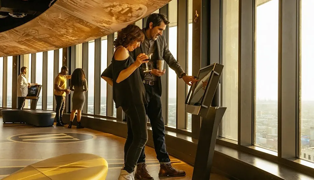 Several people are interacting with digital displays and enjoying the view from a large windowed observation area