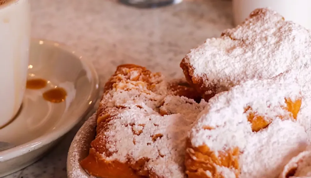 The image shows a plate of beignets dusted with powdered sugar next to a cup of coffee on a marble table