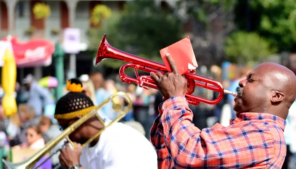 A man in a plaid shirt passionately plays a red trumpet in a bustling outdoor setting