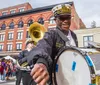 A smiling man in a marching band uniform plays a drum in a lively street parade