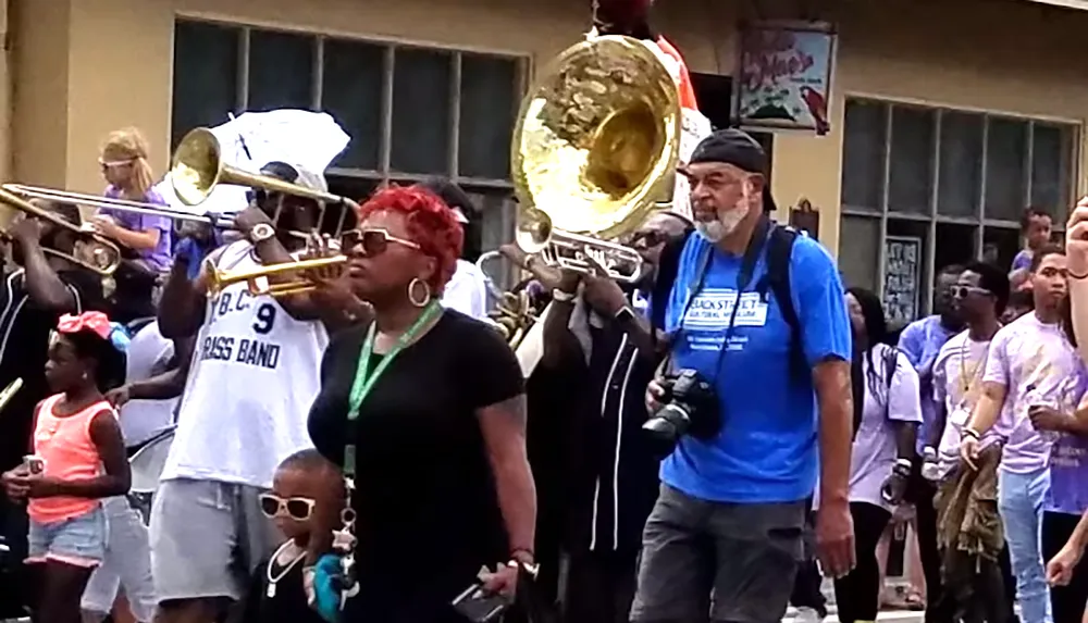 A lively street parade features musicians playing brass instruments and people walking alongside capturing the vibrant atmosphere